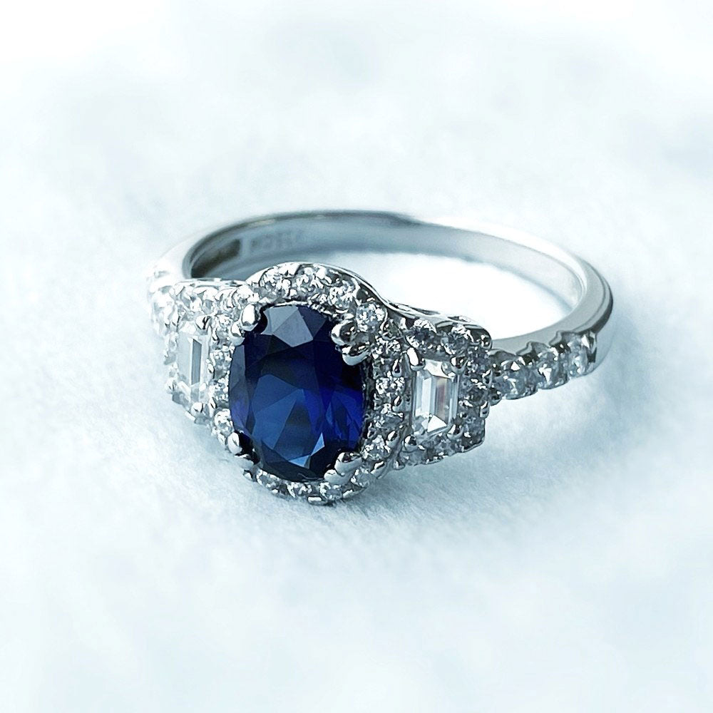 Flatlay view of 3-Stone Halo Simulated Blue Sapphire Oval CZ Ring in Sterling Silver