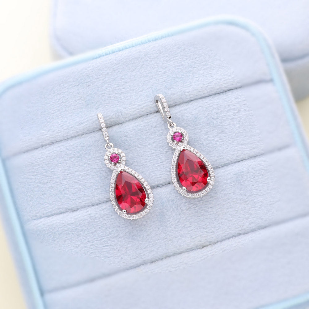 Flatlay view of Halo Simulated Ruby Pear CZ Dangle Earrings in Sterling Silver, 2 of 4