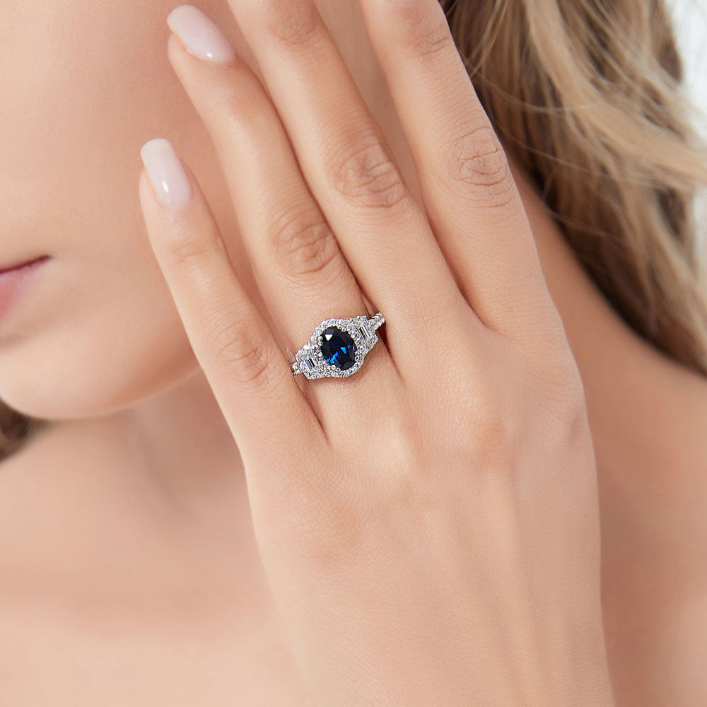 Model wearing 3-Stone Halo Simulated Blue Sapphire Oval CZ Ring in Sterling Silver