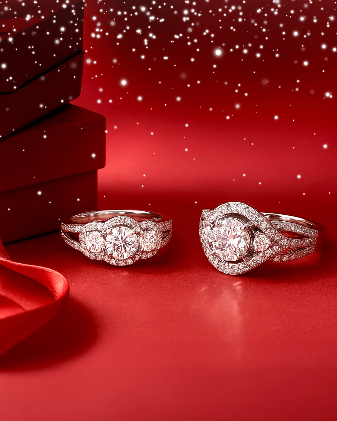 Two rings on a red surface with a red box and ribbon in the background.