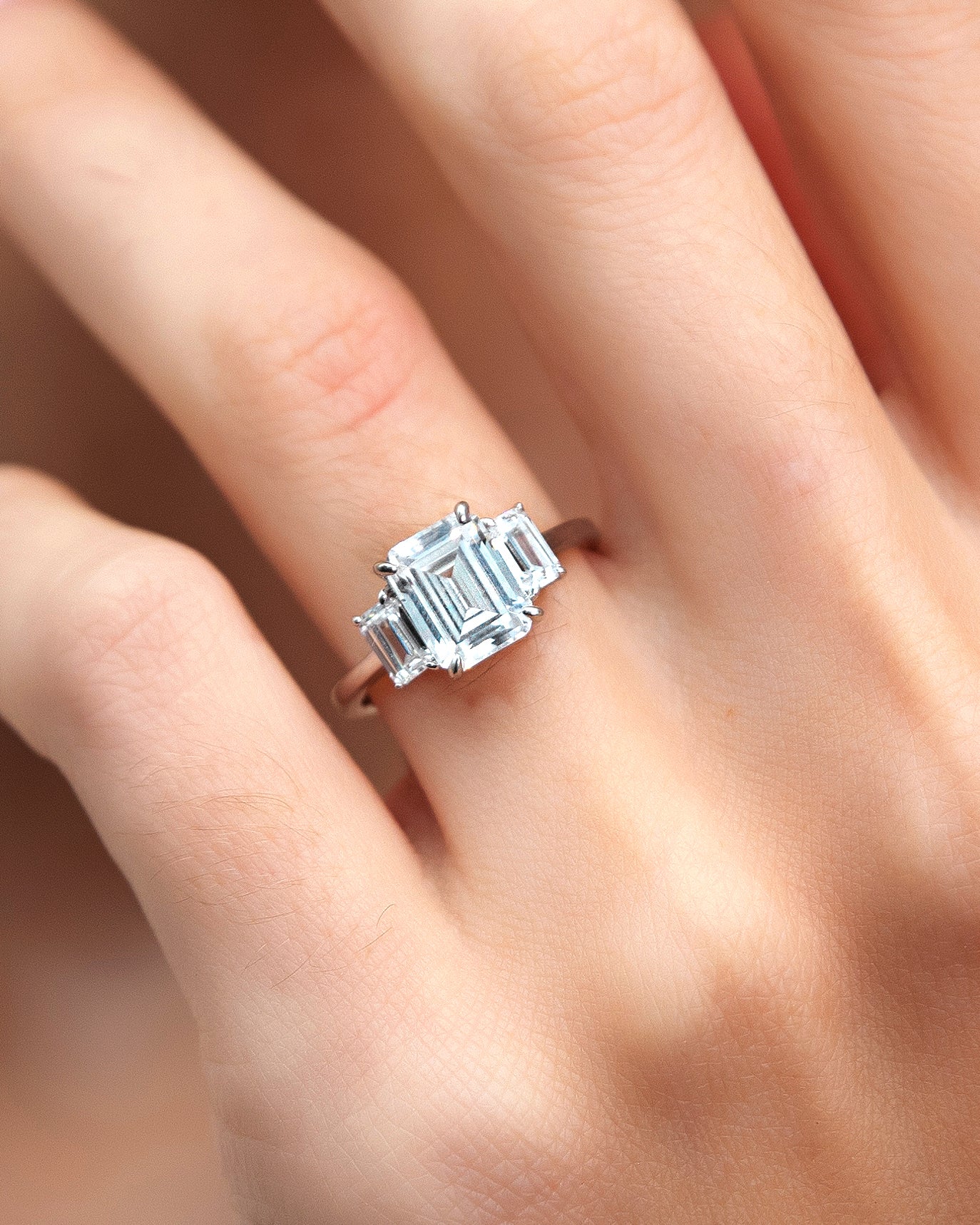 3-stone emerald ring on a finger with a soft focus background